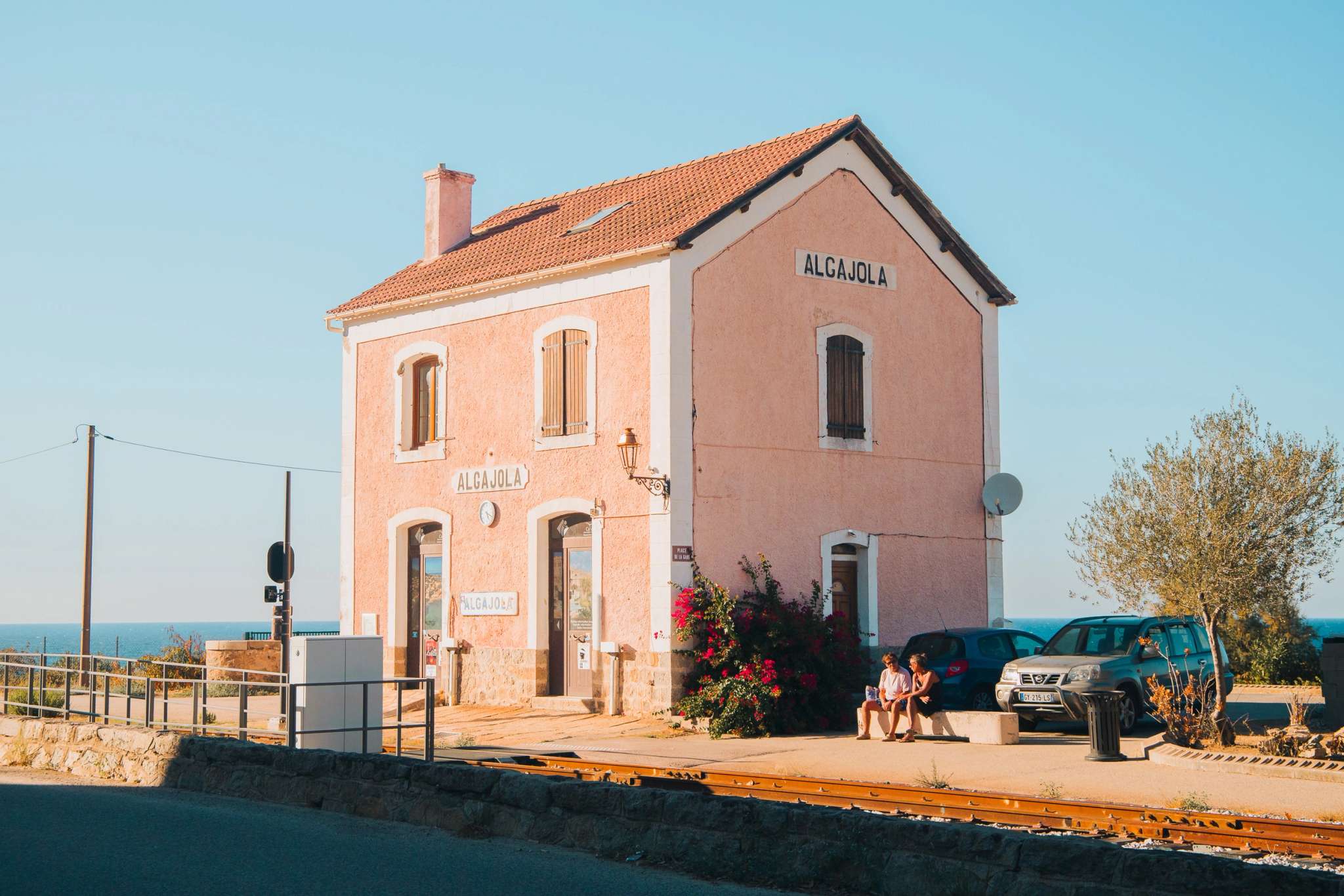 Gare d'Alcajola en Corse, bâtiment rose avec toit en tuiles, face à la mer Méditerranée