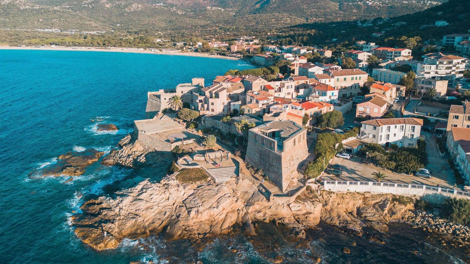 Village côtier méditerranéen avec maisons colorées sur falaises rocheuses et mer turquoise