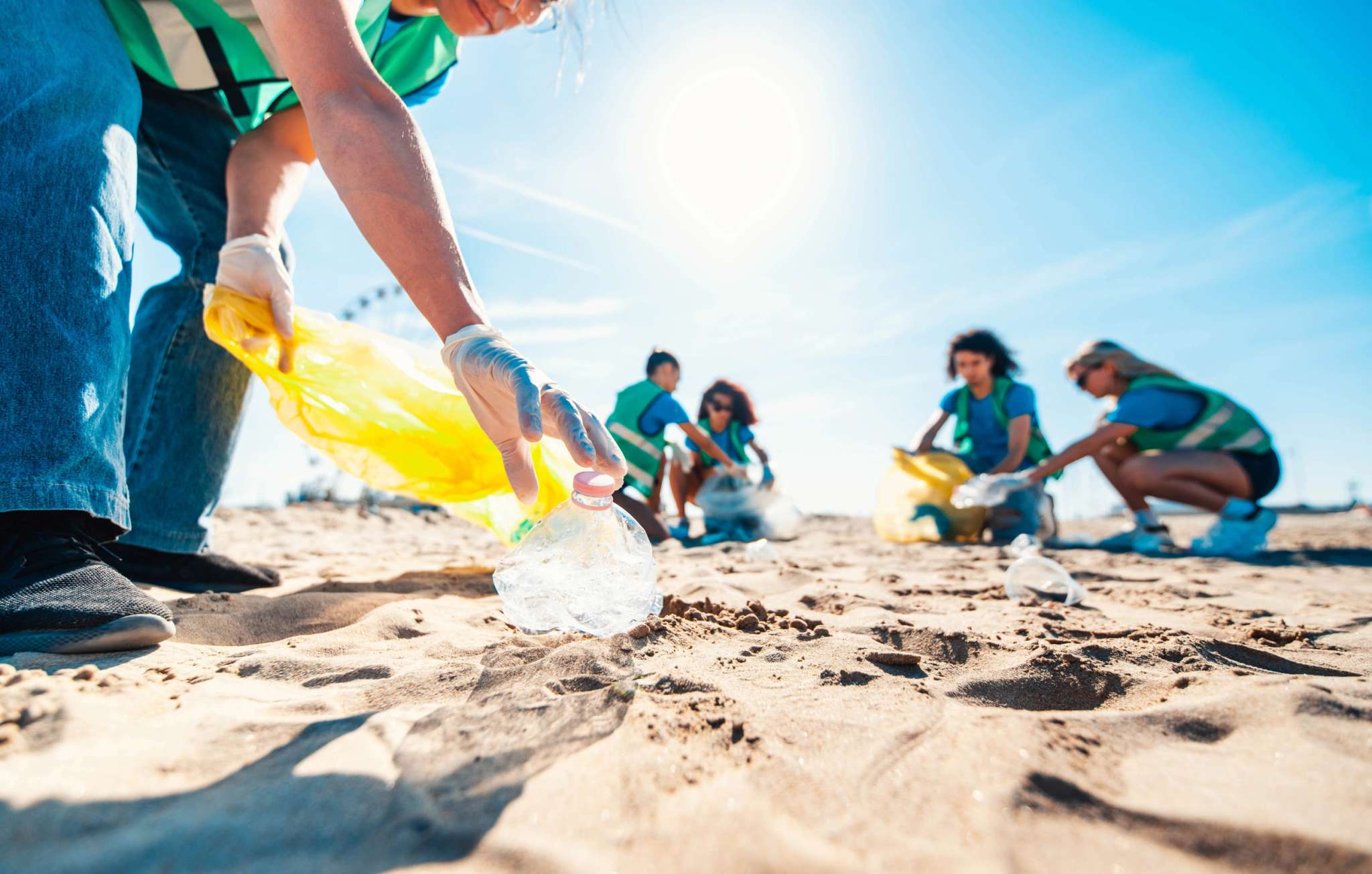 Groupe de bénévoles nettoyant une plage en ramassant des déchets plastiques sous le soleil
