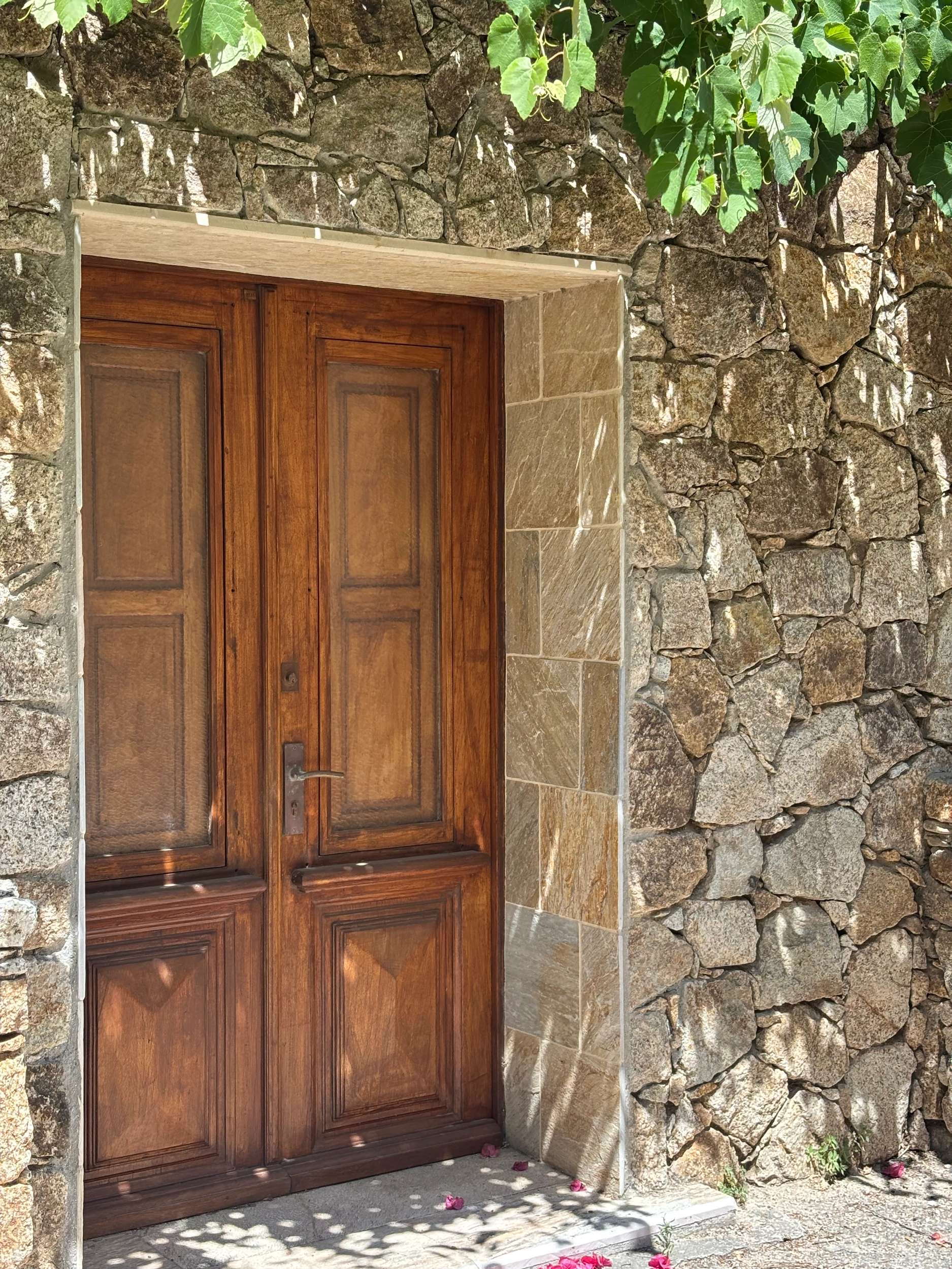 Porte en bois massif d'époque dans un mur de pierre ancienne avec lierre et fleurs